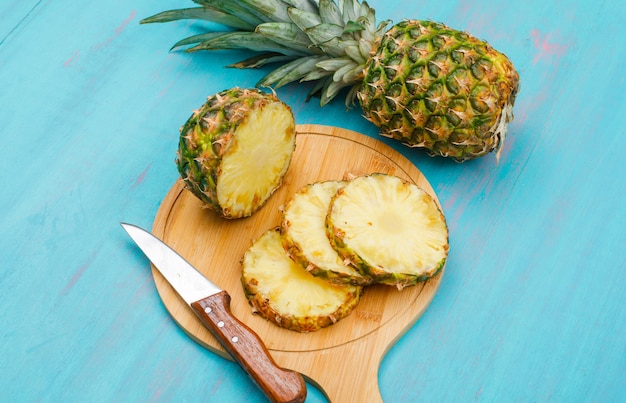 Ananas intero ed affettato con un coltello in un tagliere su ciano blu, vista dell'angolo alto.