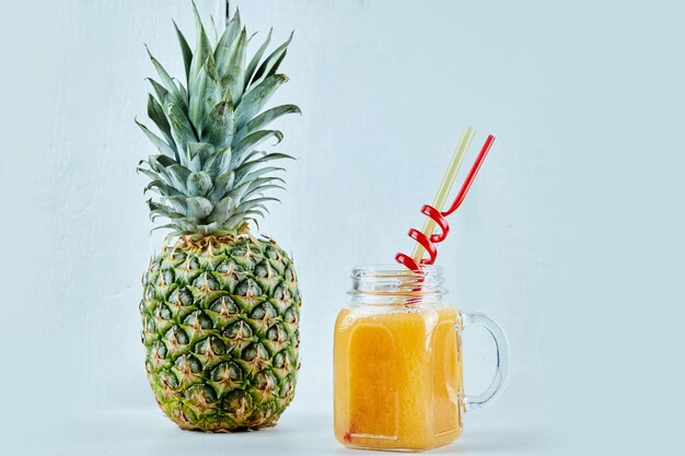 Ananas maturo e un bicchiere di succo sull'azzurro.