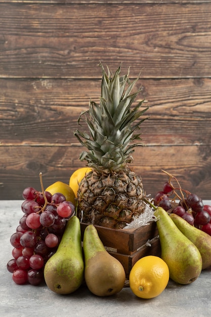 Ananas maturo in una scatola di legno con vari frutti freschi sulla superficie in marmo.