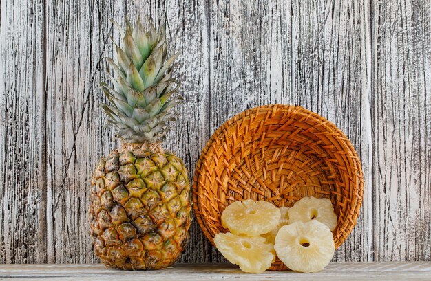 Ananas secchi con ananas fresco in un cestino su superficie di legno