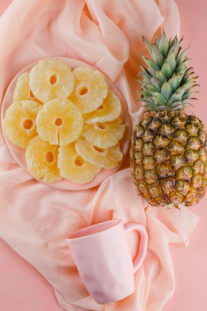 Ananas secchi in un piatto con ananas e tazza freschi sulla superficie del tessuto e di rosa