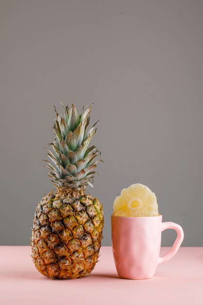 Ananas secco in una tazza con ananas fresco sulla superficie rosa e grigia