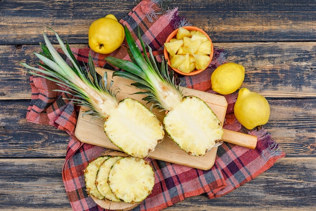 Ananas succosi affettati con due cotogne e un limone in bordi di legno e ciotola sulla vecchia superficie di legno di lerciume e panno di picnic, disposizione piana.