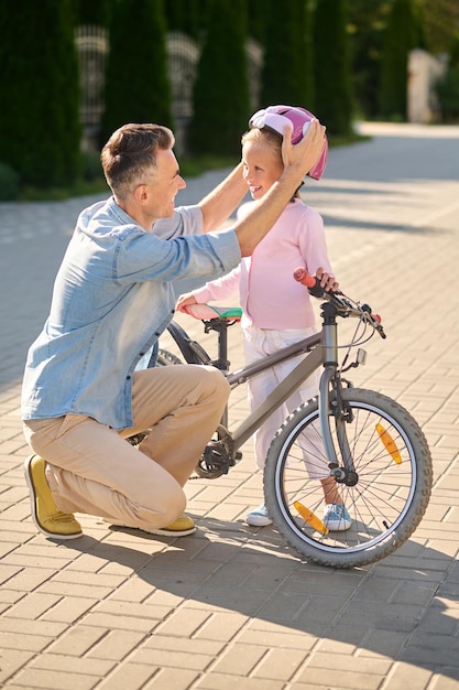 Andare in bici. Un uomo che mette un casco protettivo sulla testa di sua figlia prima di andare in bicicletta