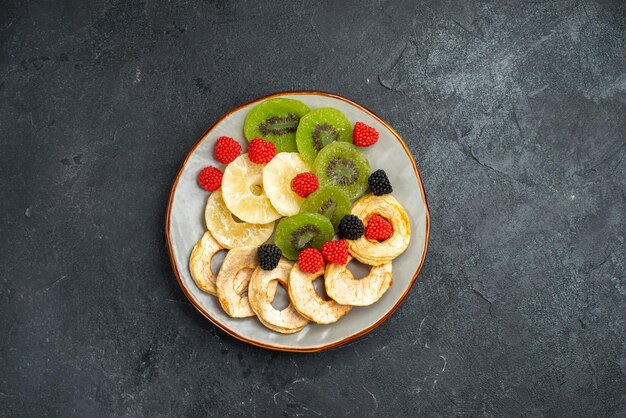 Anelli di ananas essiccati vista dall'alto con kiwi essiccati e mele sulla superficie grigio scuro