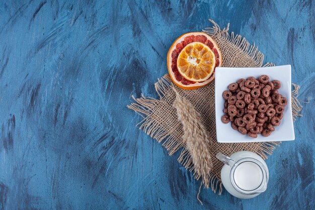 Anelli di cereali al cioccolato in un piatto bianco con frutta secca e una brocca di vetro di latte.