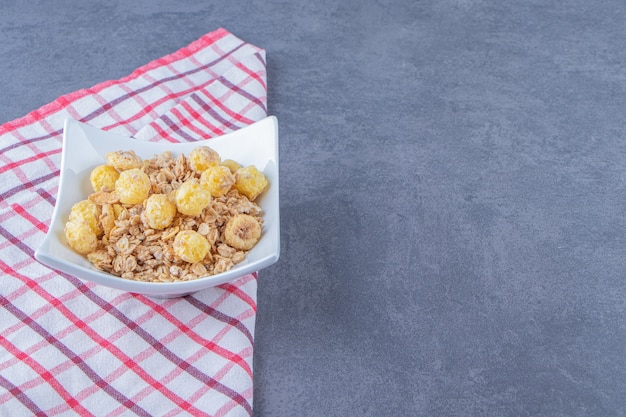 Anello di mais al miele con muesli in una ciotola su un canovaccio, sullo sfondo di marmo.