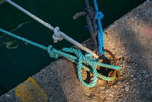 Anello di ormeggio con corda nautica blu e bianca legata montata su un molo di cemento attrezzature di sicurezza marina