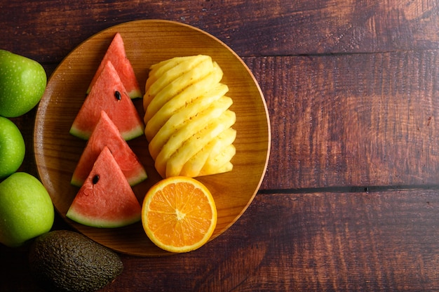 Anguria, arancia e ananas tagliati a pezzi su un piatto di legno con le mele.