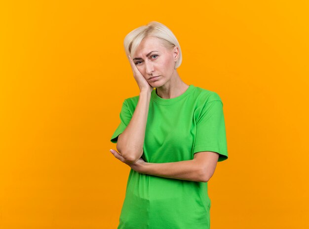 Annoiato donna bionda di mezza età guardando davanti mettendo la mano sul viso isolato sulla parete gialla