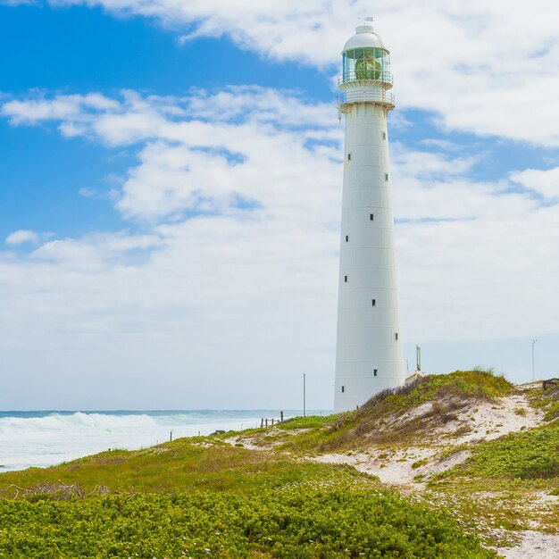 Antico faro su una riva erbosa sotto un bel cielo nuvoloso a Cape Town, Sud Africa