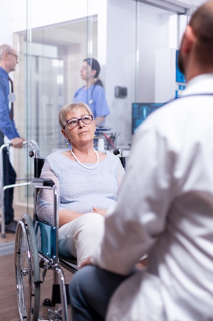 Anziana disabile seduta in sedia a rotelle durante la visita medica con il medico nella stanza d'ospedale
