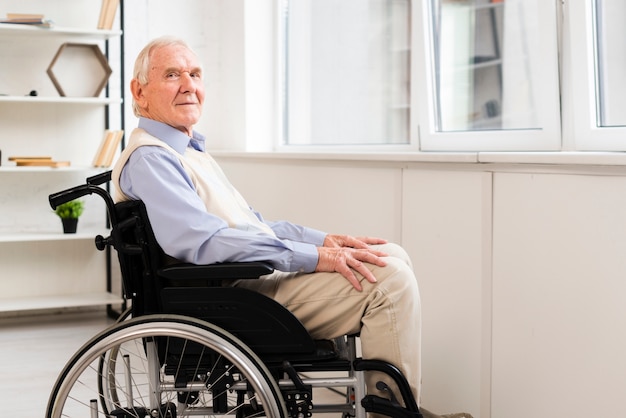 Anziano di vista laterale che si siede sulla sedia a rotelle