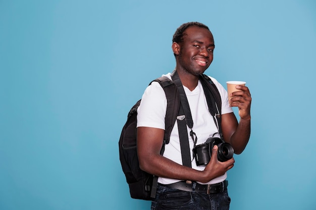 Appassionato di fotografia con dispositivo DSLR e zaino entusiasta per il viaggio del fine settimana delle vacanze. Turista con la macchina fotografica che sorseggia una bevanda mentre si prepara per il viaggio urbano. Studio girato