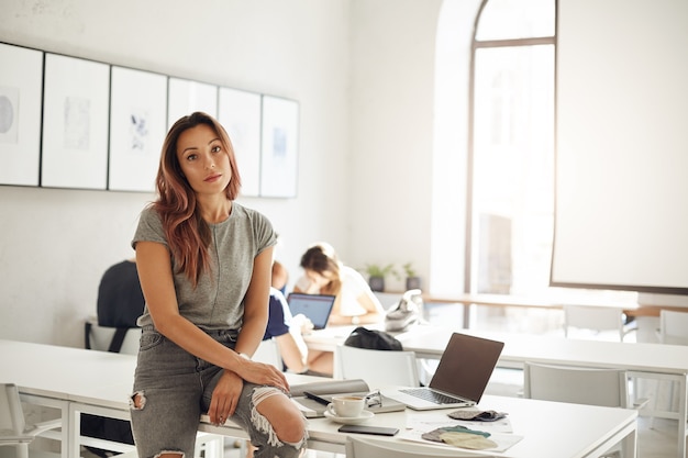 Apprendista di fashion design che studia in uno spazio di coworking o campus seduto sul tavolo con laptop e campioni tessili Concetto di professioni alla moda.