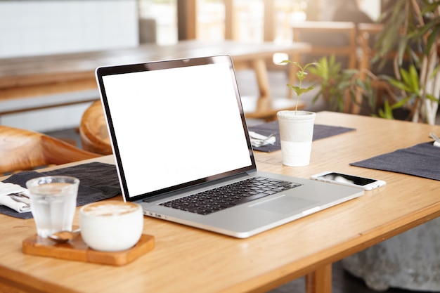 Apra il computer portatile con lo schermo bianco in bianco sulla tabella