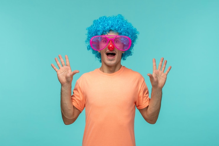 Foto gratuito april fools day ragazzo eccitato spogliato occhiali da sole rosa naso rosso capelli blu pagliaccio mani divertenti rivolte verso l'alto