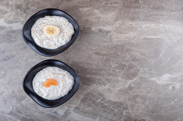 Arance a fette su una ciotola di porridge accanto alla banana a fette su una ciotola di porridge, sullo sfondo di marmo.