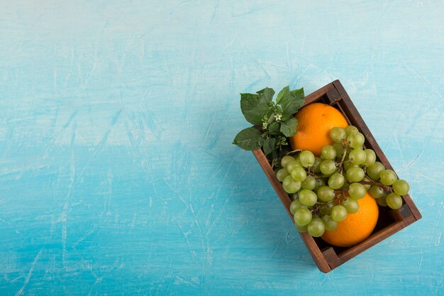 Arance gialle e un grappolo d'uva in una scatola di legno