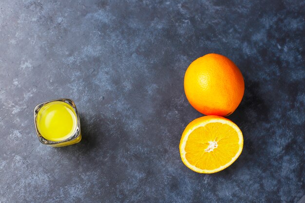 Aranciata in bicchierino con fetta d'arancia e arancio su sfondo scuro