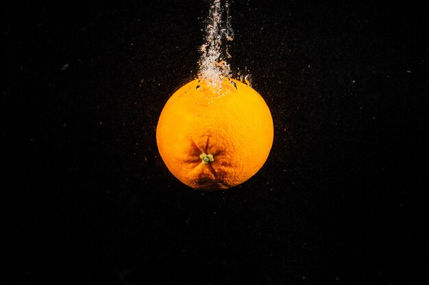 Arancio sugoso cade in acqua su sfondo nero