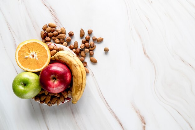 Arancione dimezzato; Mela; banana con mandorle e nocciole sulla ciotola