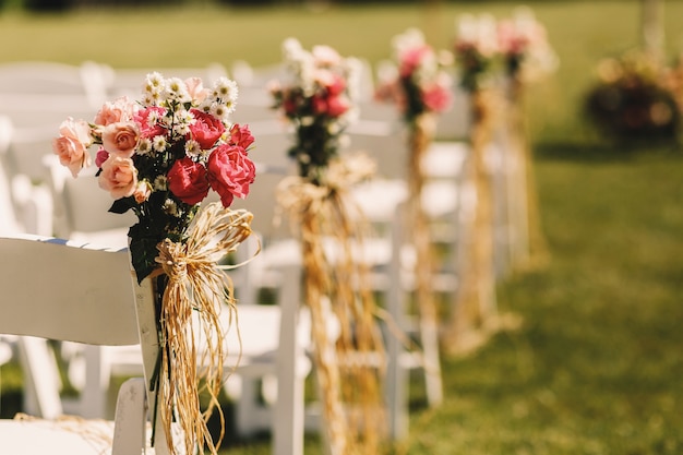 Archi di corda intrecciano mazzi di fiori rosa a sedie bianche