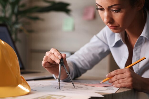 Architetto donna che lavora su nuove idee e utilizza il calibro mentre disegna piani di progetto in ufficio