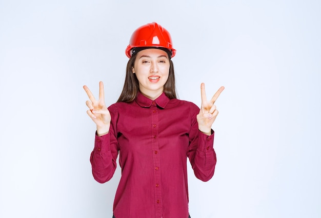 Architetto femminile di successo in casco rosso in piedi e che dà segno di vittoria.