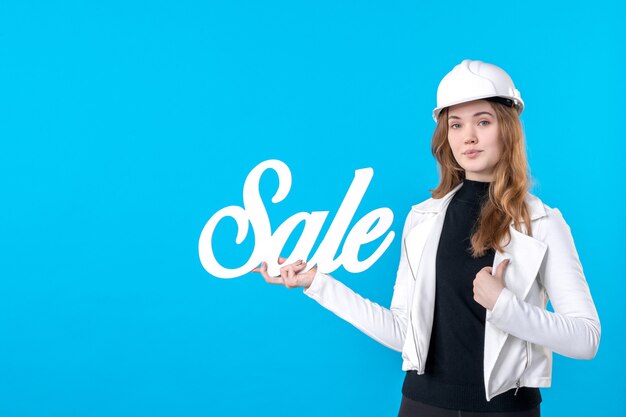 Architetto femminile di vista frontale che tiene la scrittura bianca di vendita sul blu