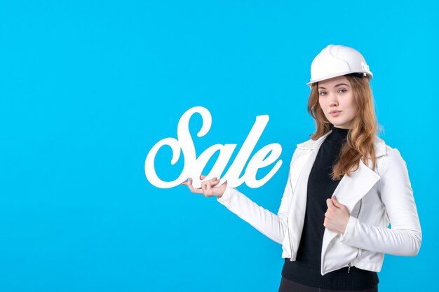 Architetto femminile di vista frontale che tiene la scrittura bianca di vendita sul blu