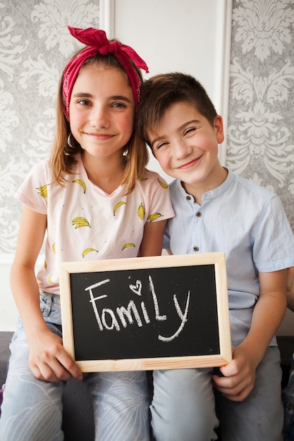 Ardesia della tenuta della sorella e del fratello piccolo con il testo della famiglia che esamina macchina fotografica