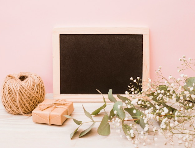 Ardesia di legno vuota con rocchetto; contenitore di regalo e fiori del respiro del bambino sullo scrittorio di legno contro fondo rosa