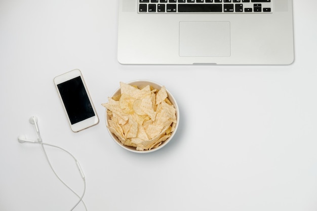 Area di lavoro con cancelleria in carta stropicciata per laptop e patatine su tavolo bianco Concetto di cattive abitudini