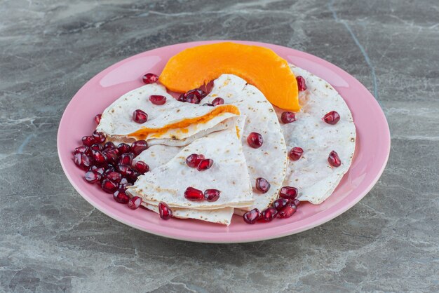 Arilli di melograno e zucca a fette con lavash su piatto, sul tavolo di marmo.