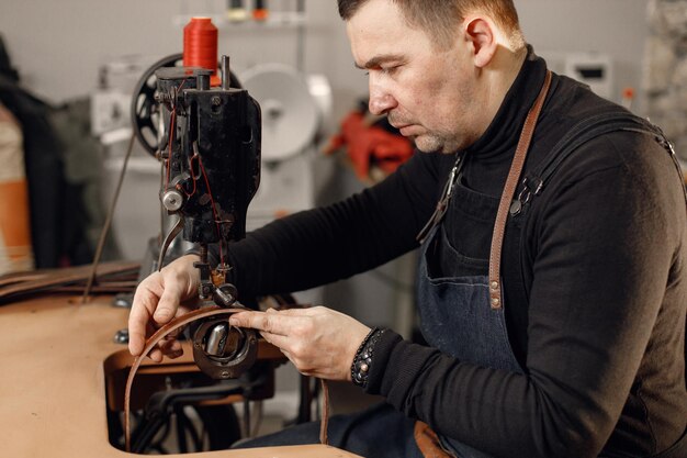 Artigiano maturo che lavora nel suo spazio di lavoro Uomo che indossa un grembiule e usa una macchina da cucire Sfondo con texture in pietra scura Grounge