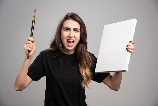 Artista femminile che grida mentre tiene il pennello e la tela.