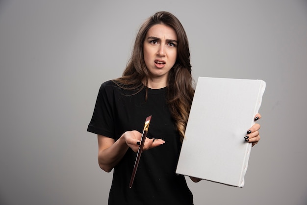 Artista femminile in camicia nera in posa con pennello e tela.