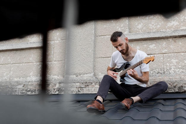 Artista maschio sul tetto a suonare la chitarra elettrica