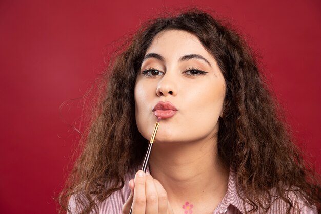 Artista riccio che osserva applicando il suo rossetto con il pennello.