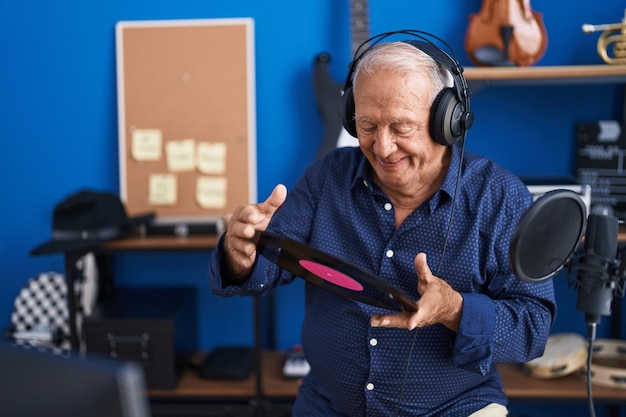 Artista senior dai capelli grigi che ascolta musica tenendo un disco in vinile nello studio musicale