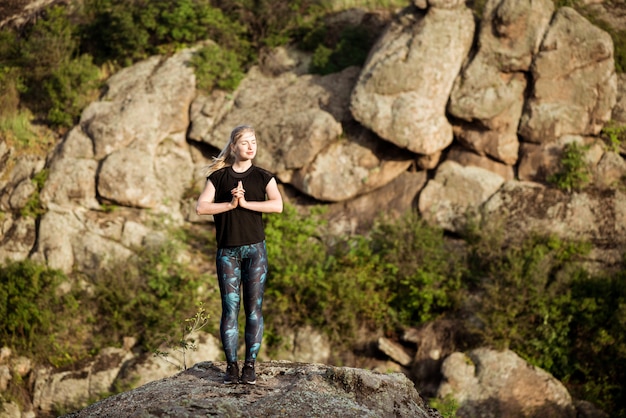 Asana di pratica di yoga della bella donna allegra su roccia in canyon