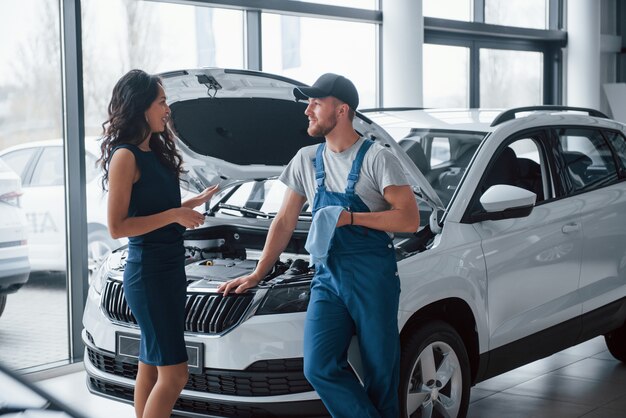 Ascoltando spiegazioni. Donna nel salone dell'auto con il dipendente in uniforme blu che riprende la sua auto riparata