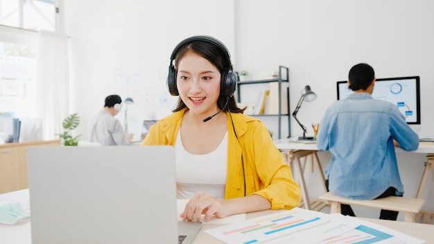 Asia imprenditrice sociale allontanamento in una nuova situazione normale per la prevenzione dei virus durante l'utilizzo di laptop presentazione ai colleghi sul piano in videochiamata mentre si lavora in ufficio. La vita dopo il virus corona.