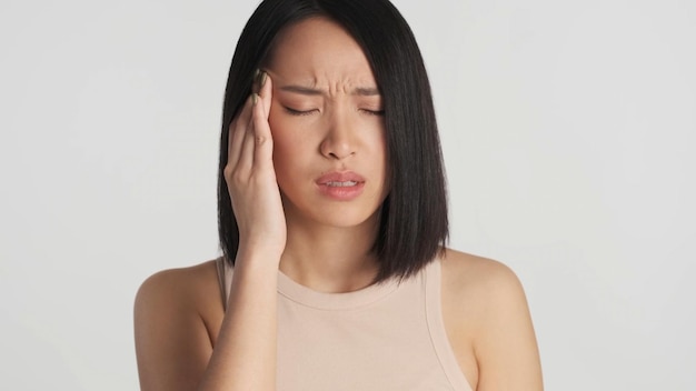 Asian mantenendo le dita sulle tempie che soffrono di mal di testa su sfondo bianco Femmina con gli occhi chiusi che sembra infelice isolata