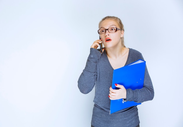 Assistente con una cartella blu che parla al telefono e sembra stressato perché qualcosa non va.