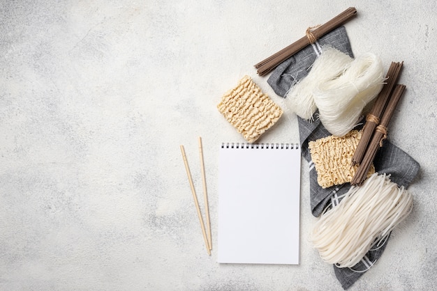 Assortimento crudo di noodles piatti laici con taccuino vuoto e copia spazio