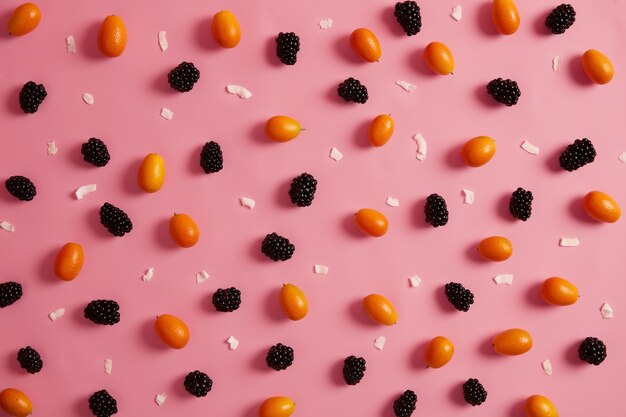 Assortimento di frutta fresca matura su sfondo rosa. Mora dolce, kumquat all'arancia e fette di cioccolato bianco intorno. Vista piana e dall'alto. Alimenti biologici succosi, vitamina C, nutrizione estiva