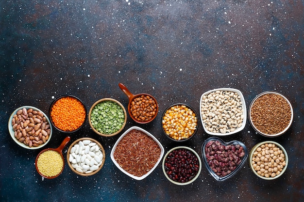 Assortimento di legumi e fagioli in diverse ciotole su fondo in pietra chiara. Vista dall'alto. Alimento proteico vegano sano.