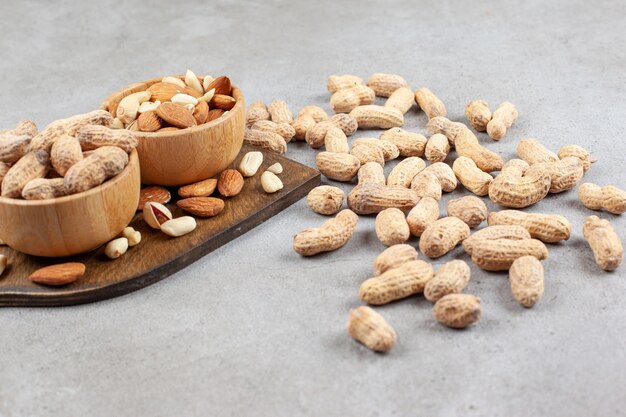 Assortimento di noci in ciotole su tavola di legno e sparse su sfondo marmo. Foto di alta qualità